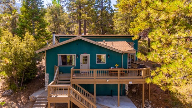 Une cabane à deux étages avec une terrasse, entourée d’arbres.