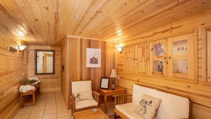 L’intérieur d’un chalet en bois comprend un canapé, des fauteuils, une petite table et un meuble avec des portes en verre.
