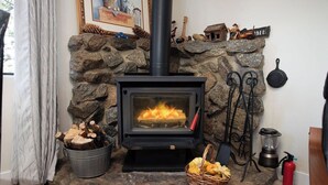 Une cheminée en pierre avec un poêle noir, un seau de bois de chauffage, un panier de citrouilles et un extincteur.