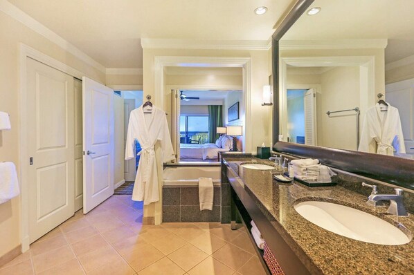 A hotel bathroom with a large mirror, two sinks, a bathtub, and a walk-in closet.