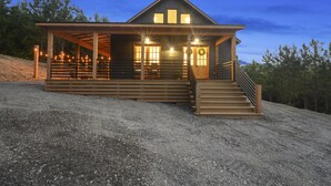 Una cabaña de madera con un porche, una escalera y una zona cubierta con guirnaldas de luces.