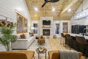 A cozy living room with a fireplace, wooden ceiling, and a dining area with bar stools.