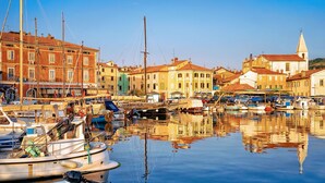 Un port de plaisance où sont amarrés des bateaux, des bâtiments aux façades rouges et jaunes, et une église dotée d’un clocher.