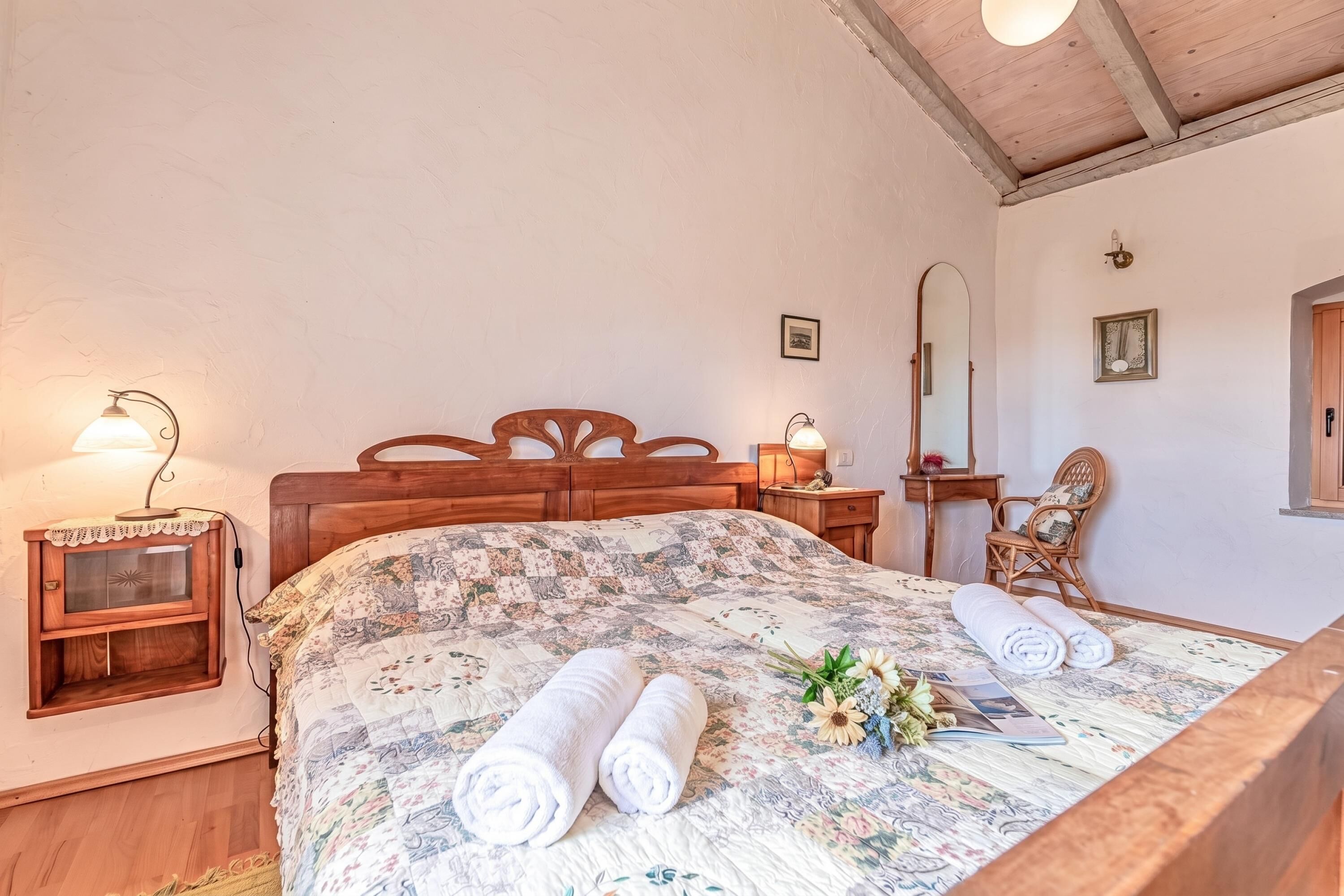 A bedroom with a wooden bed, a nightstand with a lamp, a dresser, a mirror, and a window.