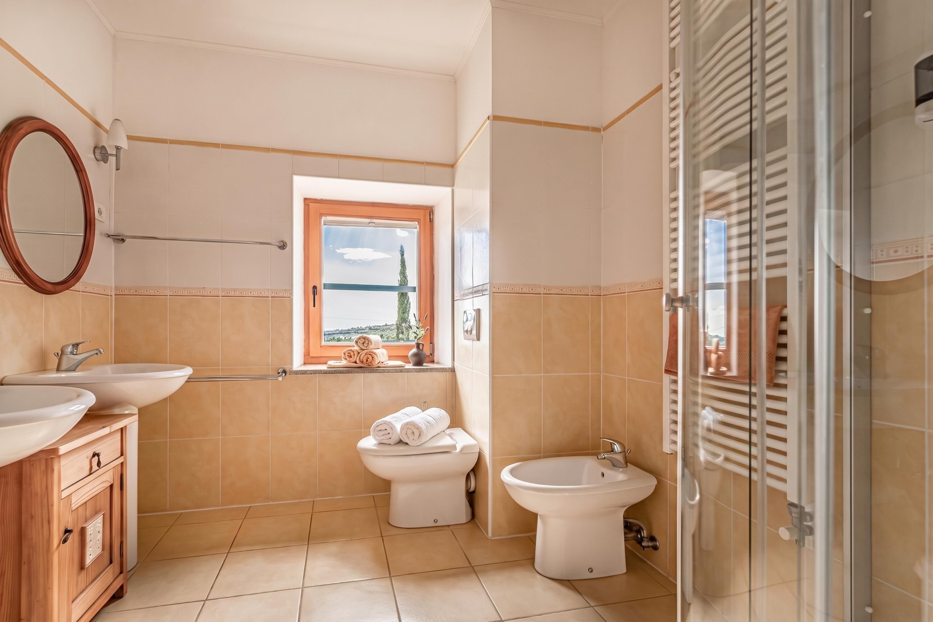Un baño con lavabo, bidé y váter. Hay una ventana con vistas al exterior.