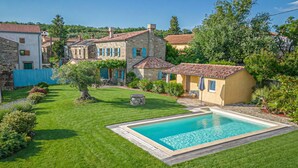 Une maison en pierre avec une piscine, entourée d’une pelouse bien entretenue et d’arbres.