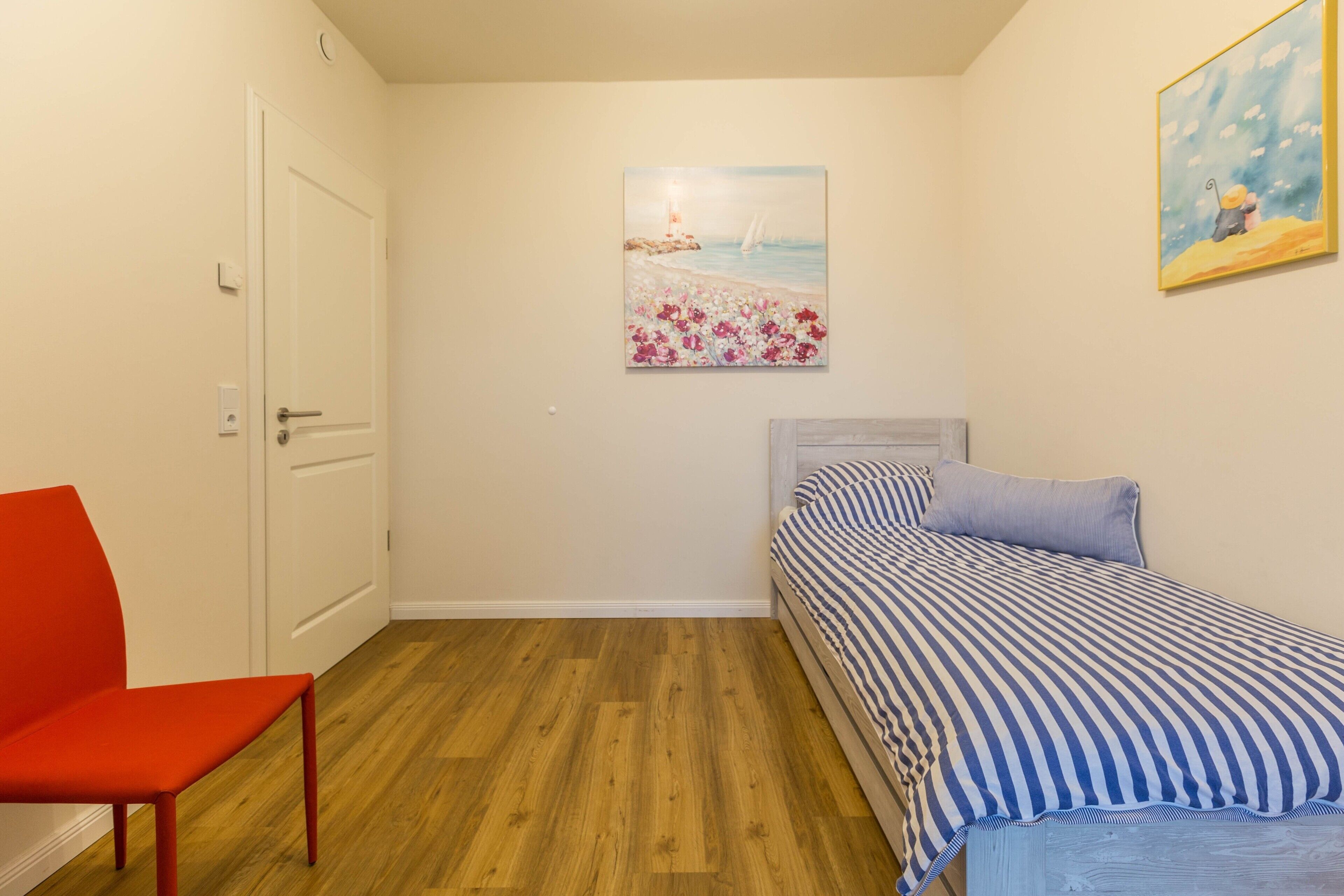 Een slaapkamer met een bed, een stoel, een deur en twee schilderijen aan de muur.