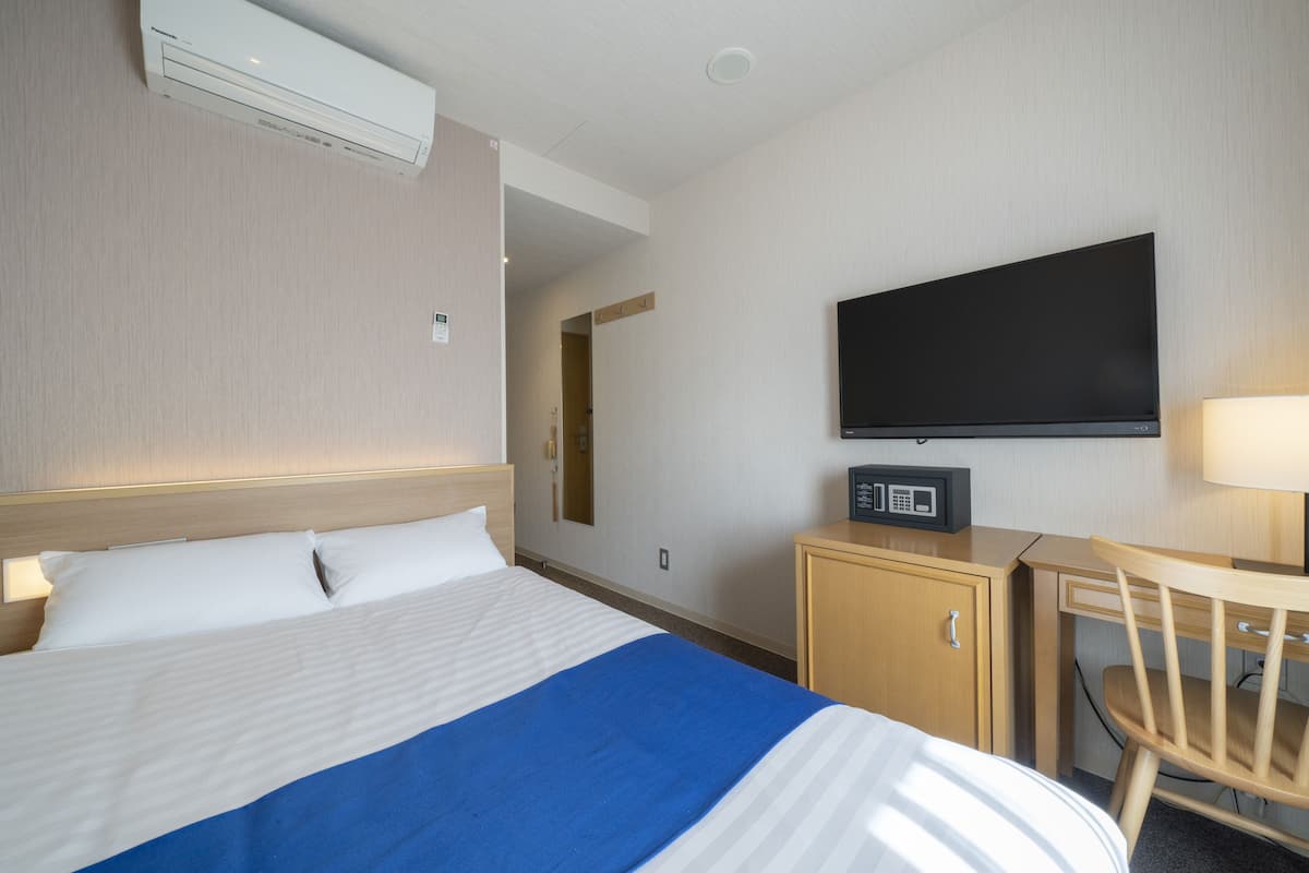 A hotel room with a bed, a television, a desk with a chair, and a microwave.