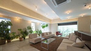 A spacious living area with a large sofa, a glass coffee table, and several potted plants. - Hotel Meriken Port Kobe Motomachi (Kobe)