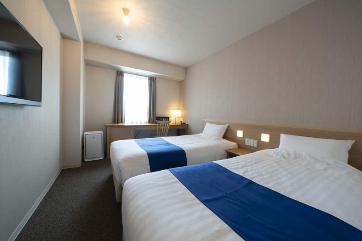 A hotel room with two beds, a desk, a chair, a TV, and a window with curtains.