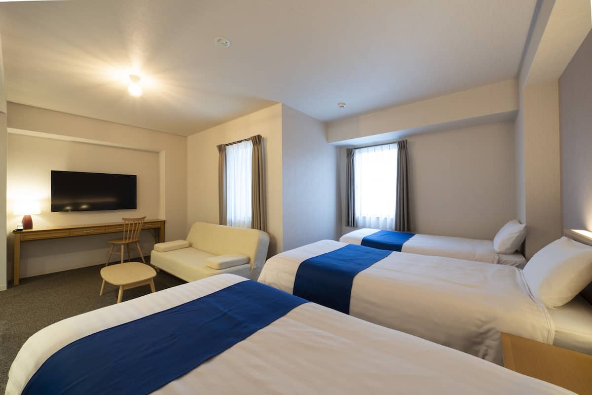A hotel room with two beds, a desk, a chair, and a TV.