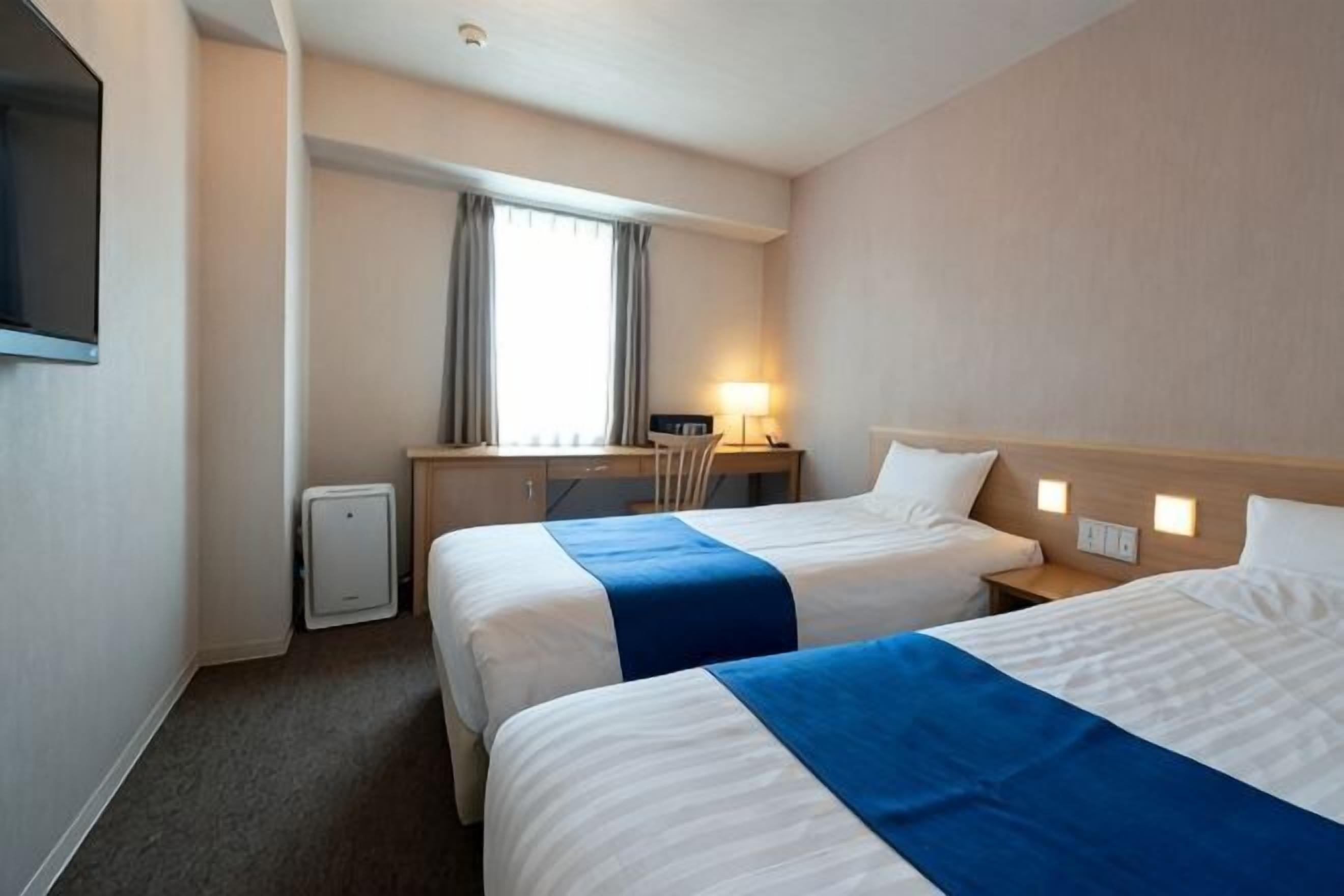 Une chambre d’hôtel avec deux lits, un bureau, une chaise, une télévision et une fenêtre avec des rideaux.