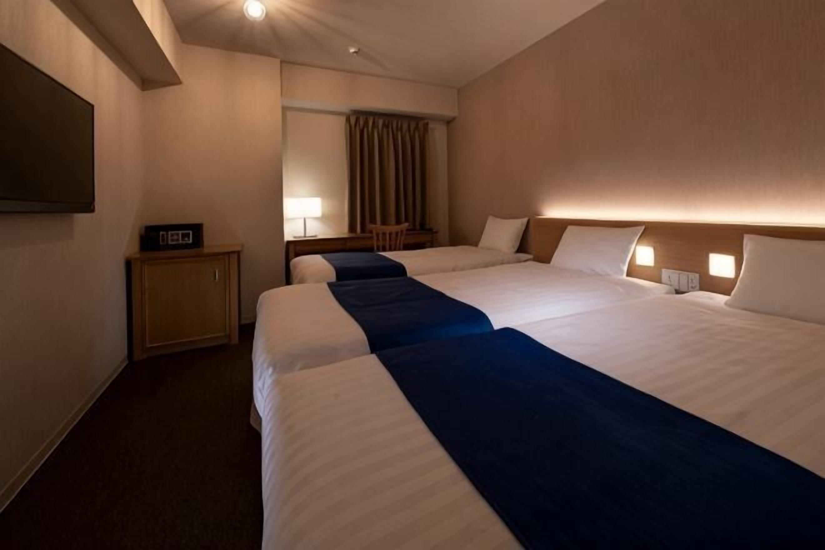 Une chambre d’hôtel avec deux lits, un bureau, une télévision et un miroir.