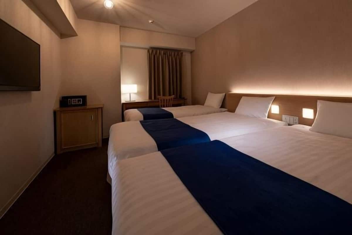Ein Hotelzimmer mit zwei Betten, einem Schreibtisch, einem Fernseher und einem Spiegel.