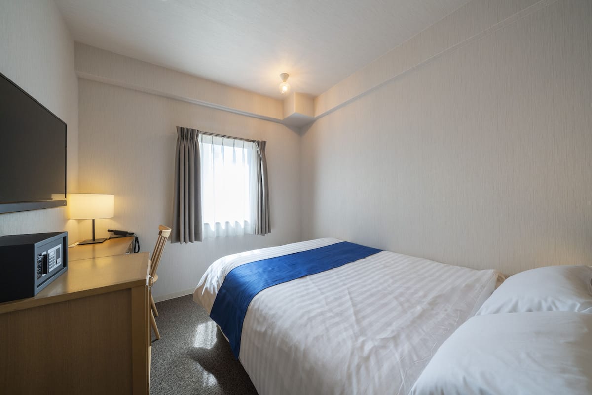 A hotel room with a bed, a desk with a lamp, a television, and a window with curtains.