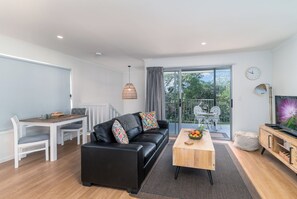 Una sala de estar moderna con un sofá de cuero negro, una mesa de centro de madera y un comedor con sillas blancas.