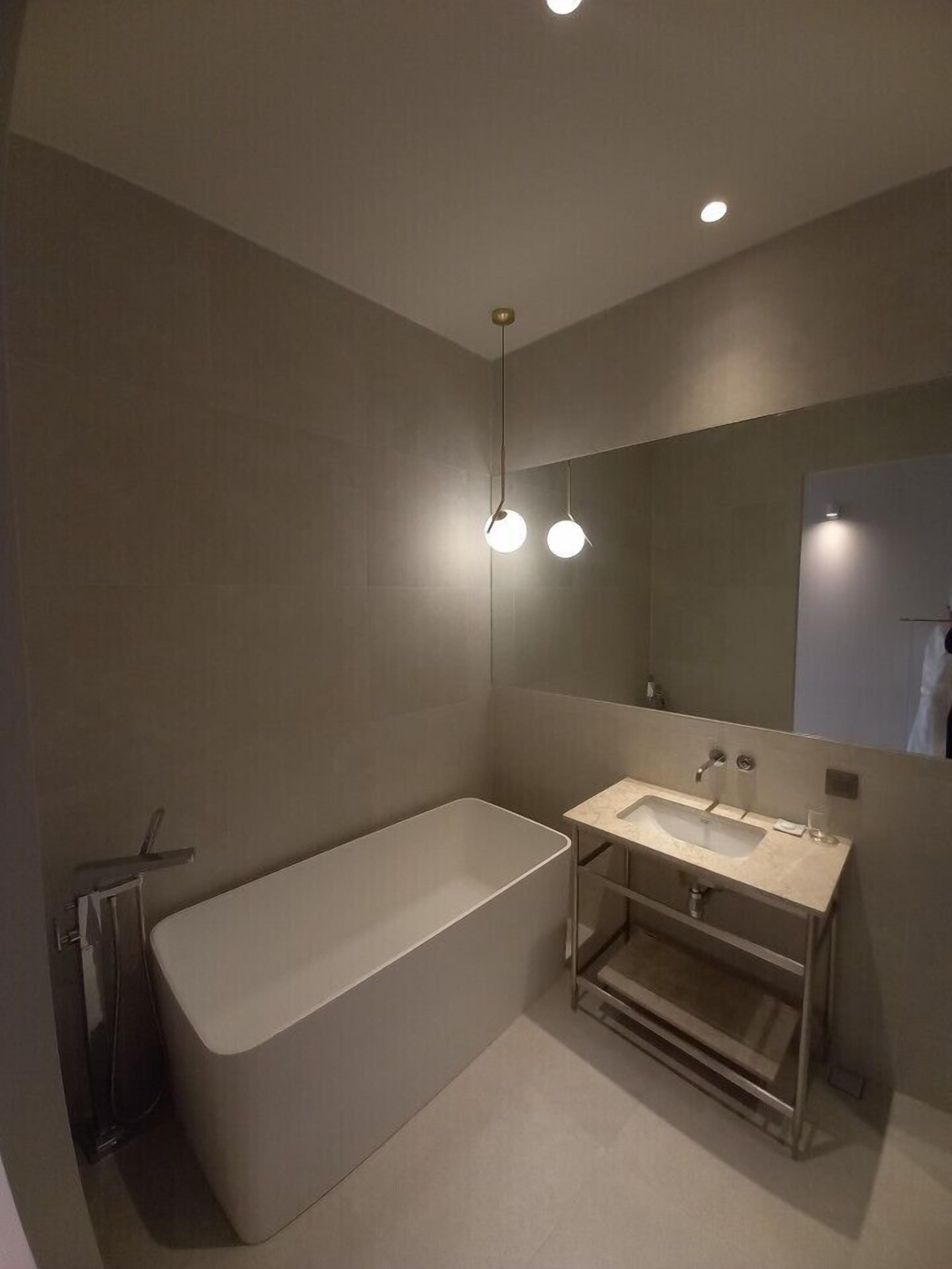 Un baño moderno con una bañera independiente, tocador con espejo e iluminación empotrada.