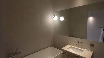 Un baño moderno con una bañera independiente, tocador con espejo e iluminación empotrada.