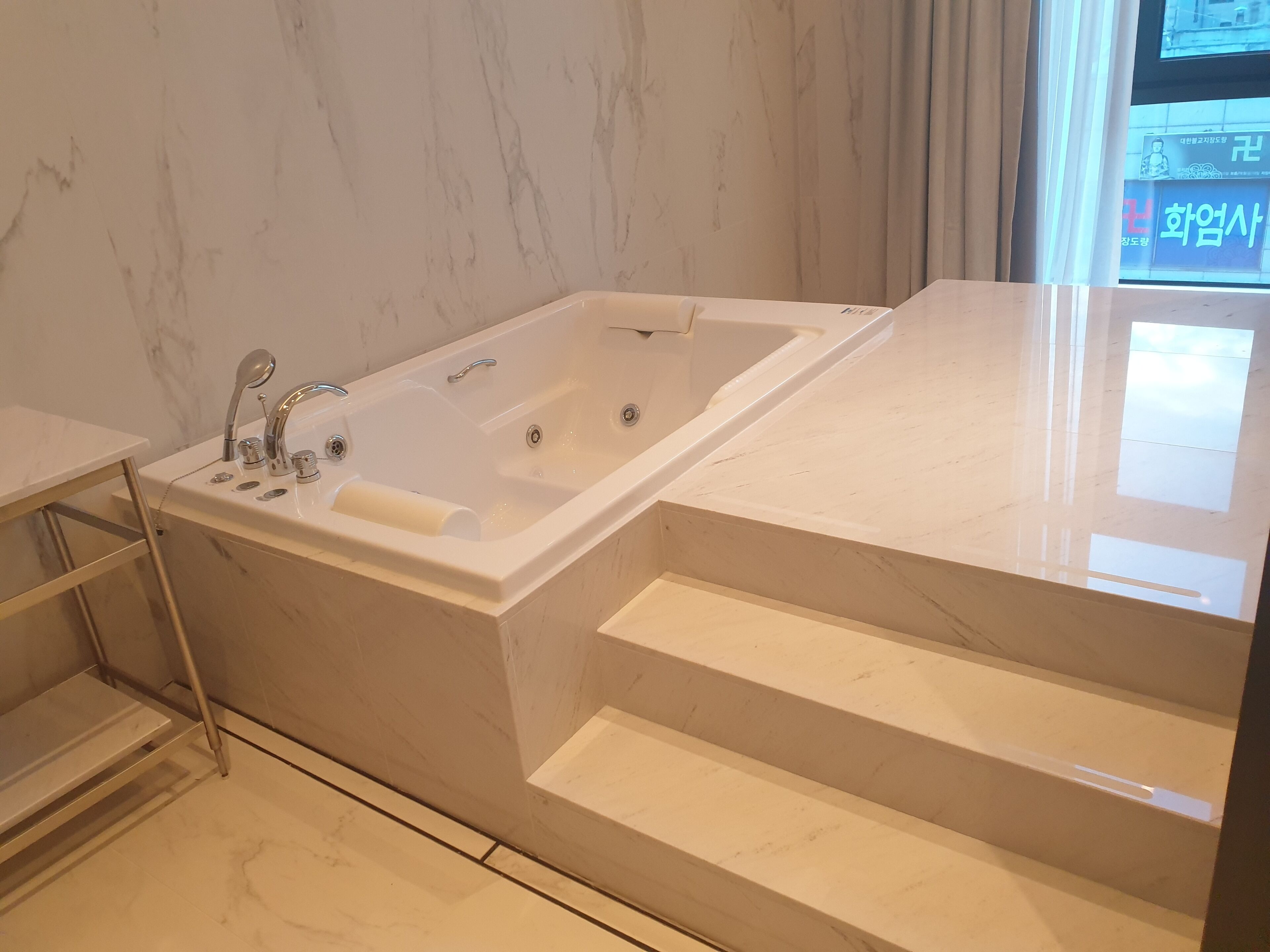 Ein modernes Badezimmer mit einer großzügigen Badewanne, Marmorböden und einem Fenster mit Blick nach außen.