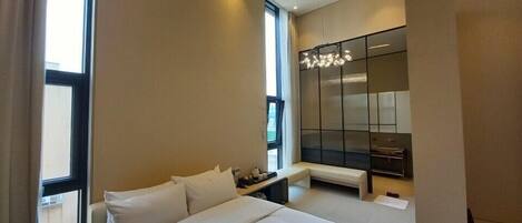 A modern hotel room with a large bed, a small table, a seating area, a large mirror, and a view of the city.