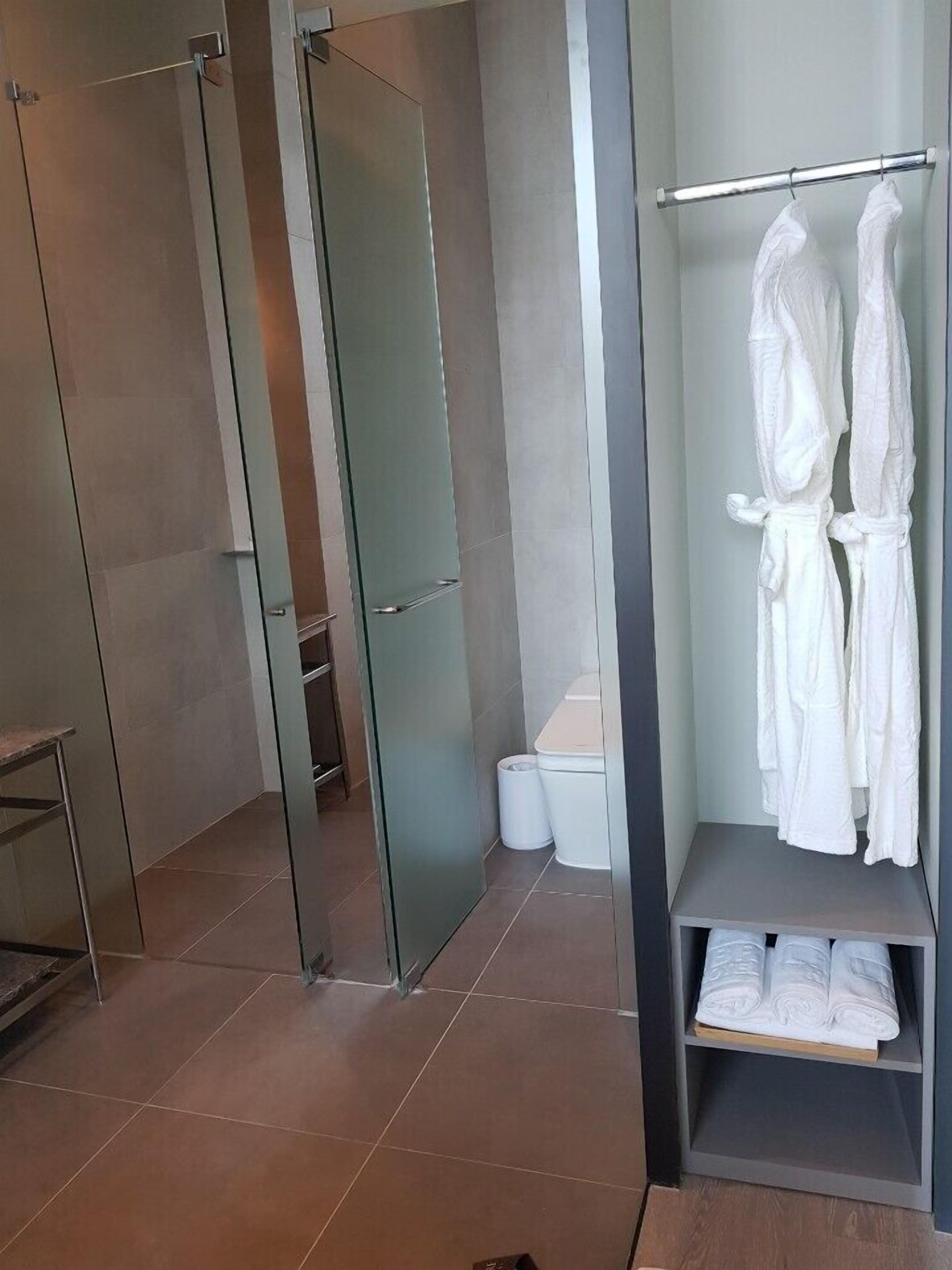 A modern bathroom with a glass shower enclosure, a towel rack with white towels, and a small shelf with folded towels.