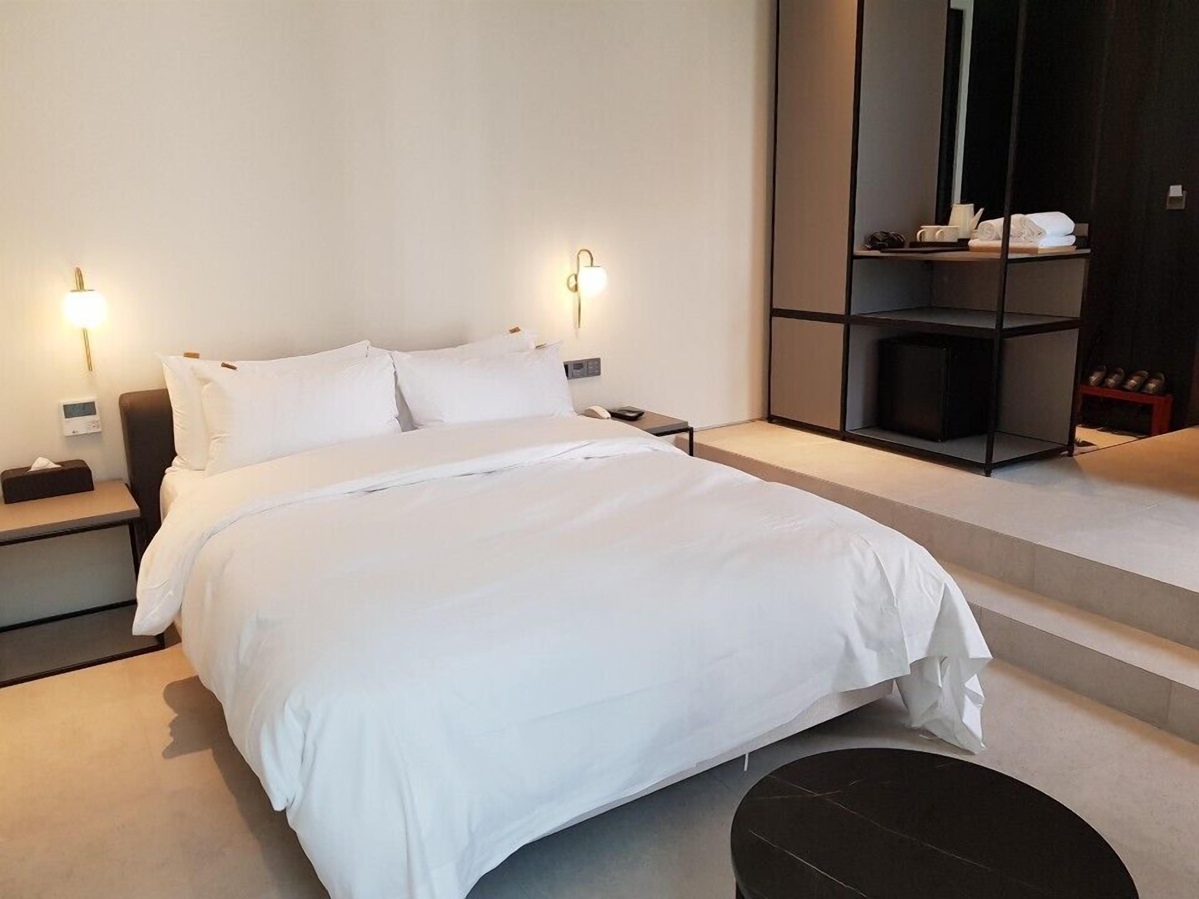 Una habitación de hotel moderna con una cama grande, mesitas de noche, un estante empotrado con artículos de aseo y un espejo amplio.