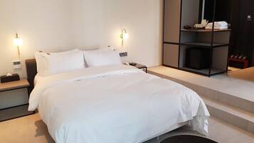 Una habitación de hotel moderna con una cama grande, mesitas de noche, un estante empotrado con artículos de aseo y un espejo amplio.