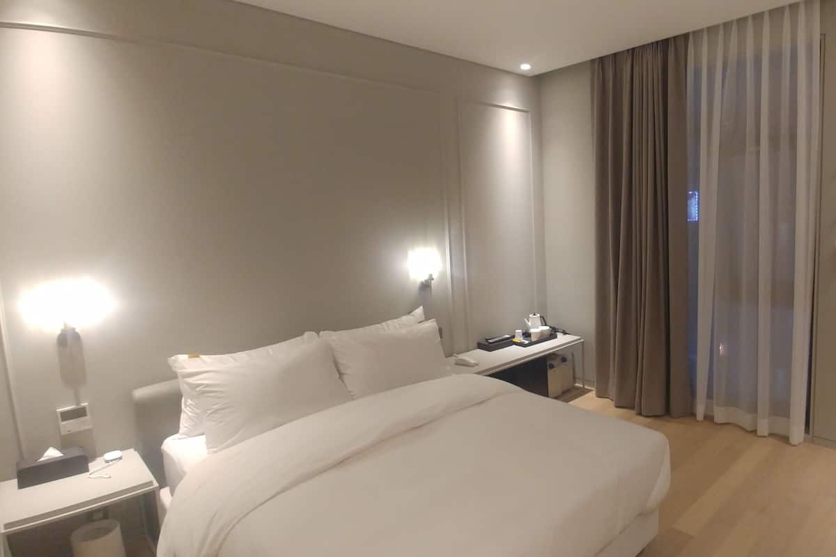 A hotel room with a bed, bedside table, lamp, and a desk with a chair.