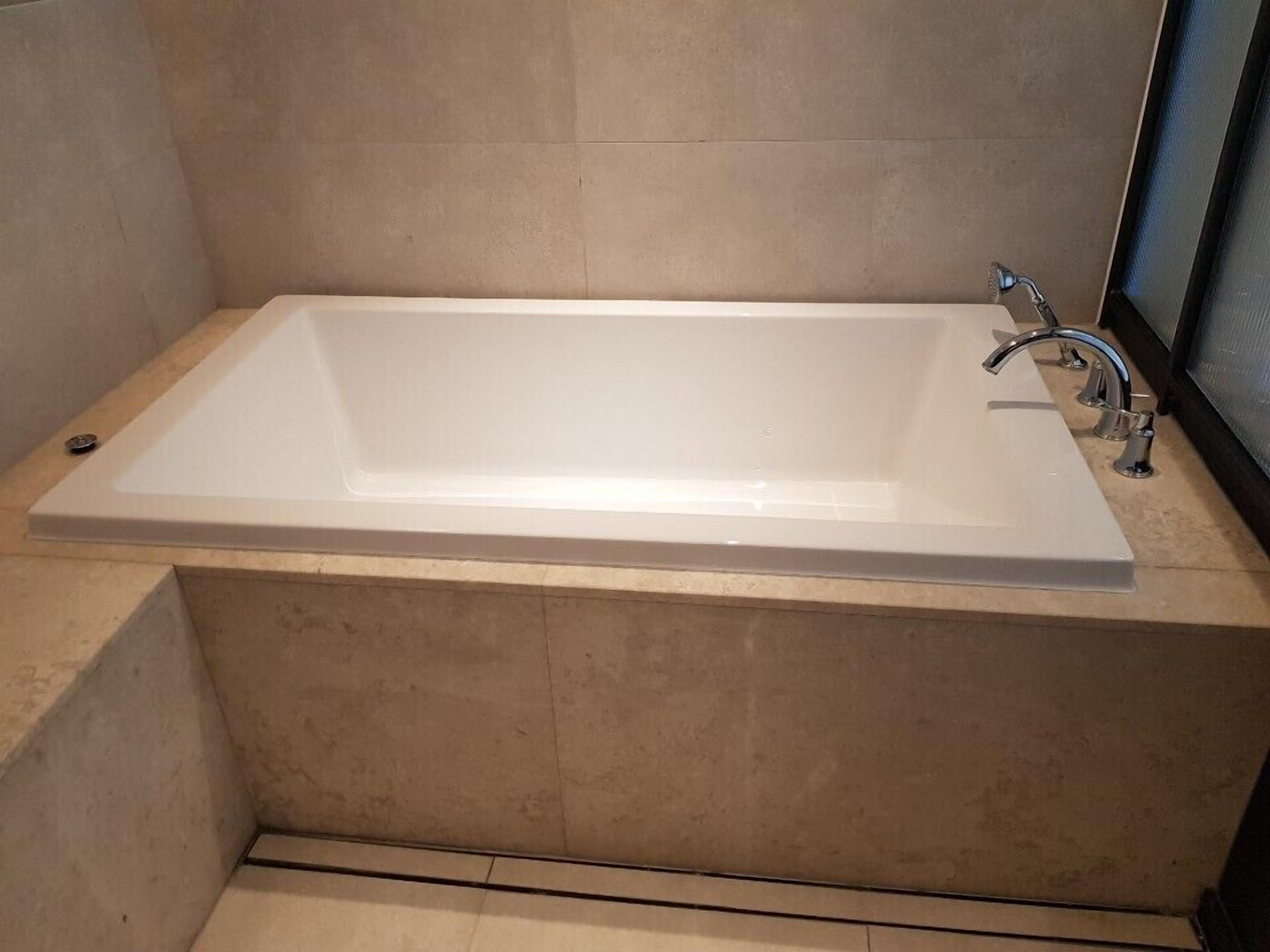 Un baño moderno con una bañera rectangular, un solo grifo y suelo de baldosas.