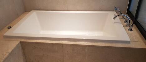 Un baño moderno con una bañera rectangular, un solo grifo y suelo de baldosas.