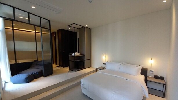 A modern hotel room with a large bed, a seating area with a sofa and a small table, a wardrobe, and a built-in TV. - Hotel Libre (Siheung)
