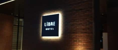 Un letrero iluminado que dice 'LIBRE HOTEL' sobre un muro de ladrillo de noche.