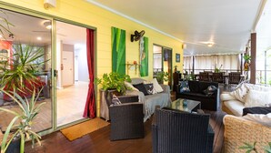 Een ruime woonkamer met rieten meubilair, een glazen deur naar een keuken en een balkon met zitplaatsen.