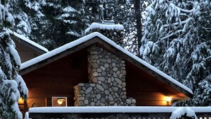 Eine Lodge mit Kamin aus Stein, einer Holzterrasse und verschneiter Umgebung.