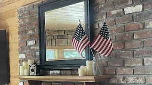Ein Kamin aus Ziegelsteinen mit einem Spiegel darüber, zwei amerikanische Flaggen und ein kleines Regal mit Kerzen und einer Kamera.