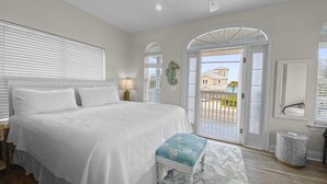 A bedroom with a large bed, a ceiling fan, a window with blinds, a door leading to a balcony, and a small table with a lamp. - "SummerTowne 1-At Pier Park"| Amazing Ocean Views | Dog-Friendly | Community Pool (Panama City Beach)
