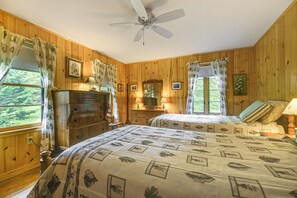 A wooden-paneled bedroom with two beds, a dresser, a ceiling fan, and a window with curtains. - Lakefront Escape w/ Deck & Kayaks in Lovell! (Lovell)