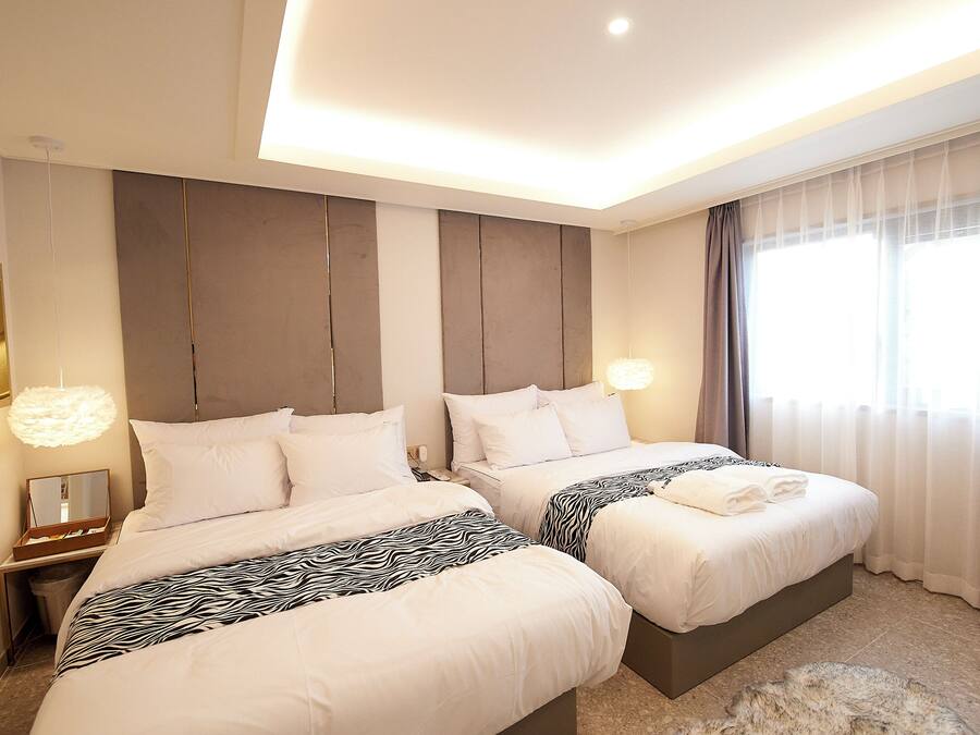 Habitación de hotel con dos camas, una mesita de noche, un espejo y un ventanal grande con cortinas.