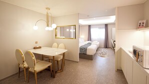 A hotel room with a dining area, a bed with a zebra print blanket, a bathroom with a sink and mirror, and a ceiling fan. - Den Basta Hotel (Busan)