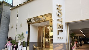 A hotel entrance with a modern facade, a sign reading "Den Basta," and a parking area visible in the background. - Den Basta Hotel (Busan)