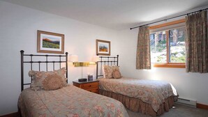 A bedroom with two beds, a nightstand, a lamp, a window with curtains, and two framed pictures on the wall. - Sagebrush, Ski in/out, hot tub, dog friendly (Gunnison)