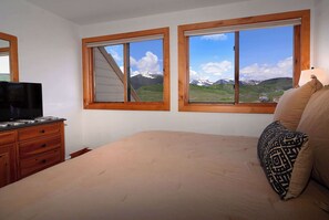 Une chambre à coucher avec un lit, une commode et deux fenêtres donnant sur la montagne.