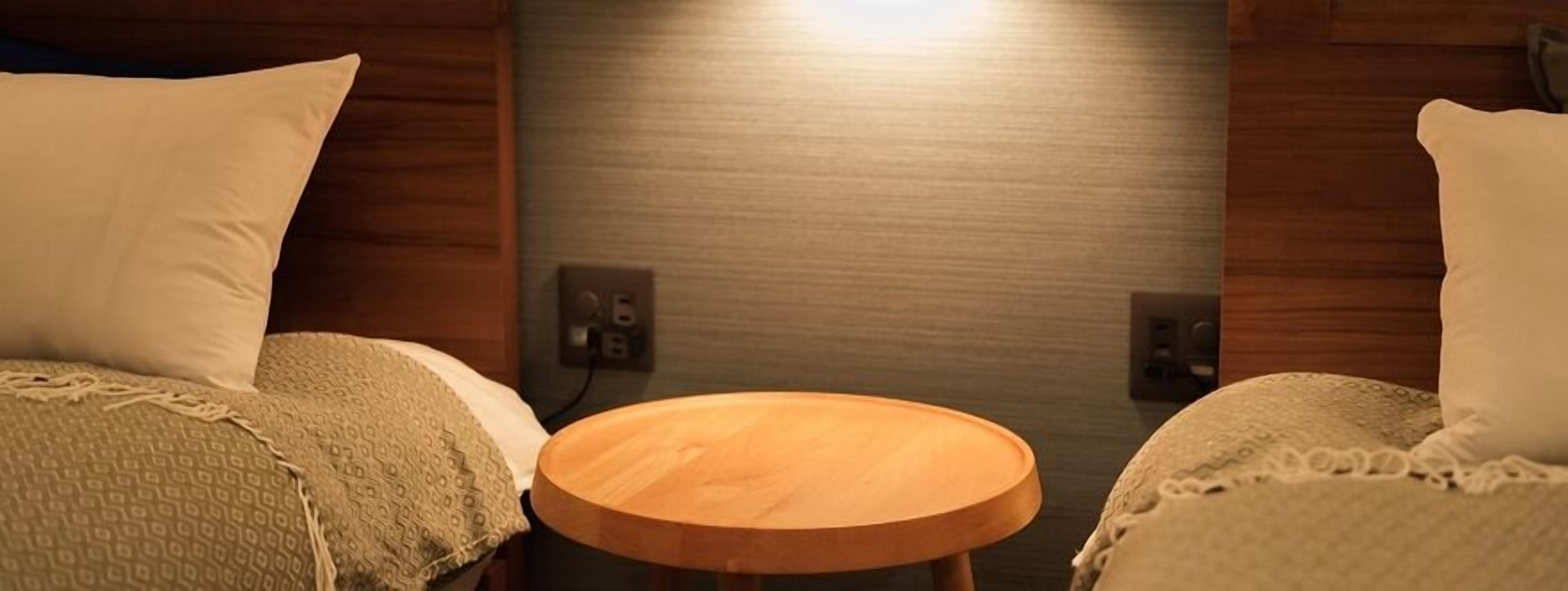 A room with two beds, a small wooden table, and a wall-mounted light fixture.