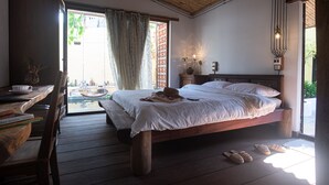 Ein Schlafzimmer mit einem hölzernen Bett, einem Schreibtisch mit Büchern, einem Stuhl und Blick ins Freie.