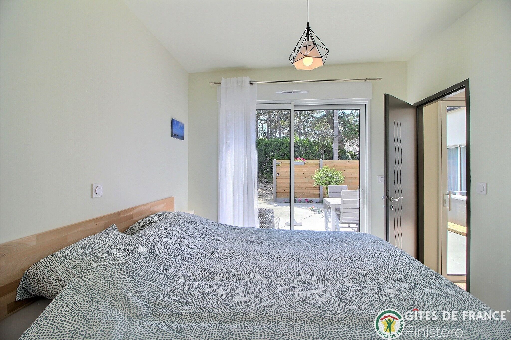 A bedroom with a bed, a ceiling light, and a sliding glass door leading to an outdoor area.