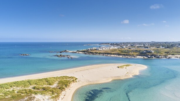 Vue aérienne d’une zone côtière avec des eaux d’un bleu limpide, des plages de sable et une petite ville avec des bâtiments.
