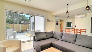 Un salon moderne avec un canapé d’angle gris, une table à manger en bois avec des chaises, et une porte-fenêtre coulissante donnant sur un patio équipé d’un jacuzzi.