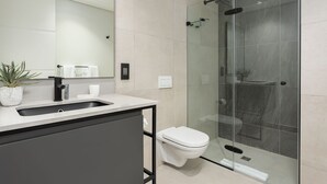 Et moderne badeværelse med en glasafskærmet brusekabine, en hvid vask og et toilet.