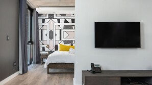 Et moderne hotelværelse med en seng, et skrivebord med telefon, et fladskærms-tv og en væg med et mønster.