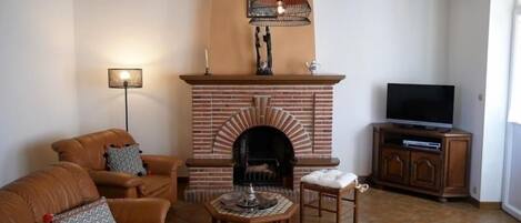 A living room with a brick fireplace, leather sofas, a coffee table, and a television on a wooden cabinet.